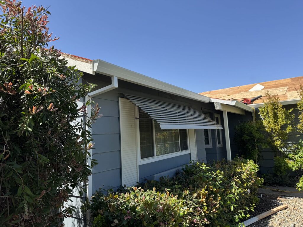 Front of the home, featuring a window with a stripped sun cover. There are newly installed gutters and downspouts.