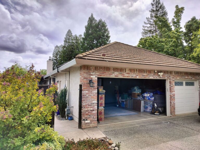 A brick house with an open garage. Brown and white gutters wrap around the perimeter of the home. A grey car is partially photographed