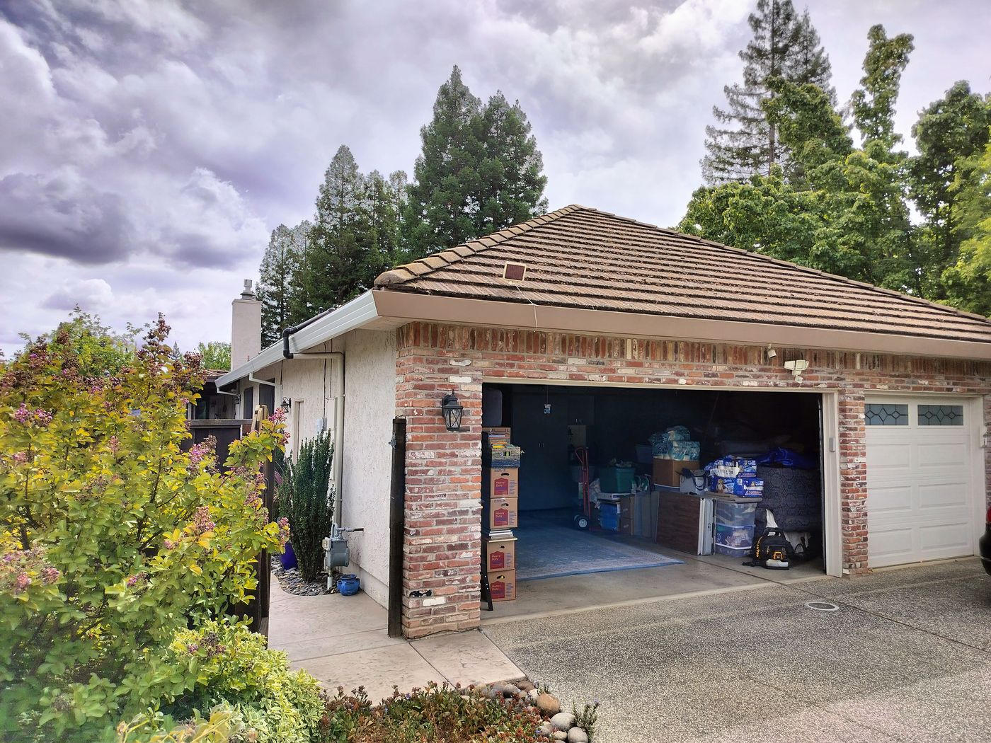 A brick house with an open garage. Brown and white gutters wrap around the perimeter of the home. A grey car is partially photographed