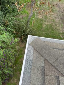 Close-up of newly installed gutter guards in the corner. Background features the grass and some plants.
