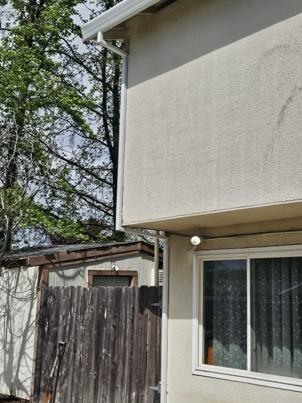 Two-story home with a clean, stucco exterior with new downspouts installed at the back of the home.