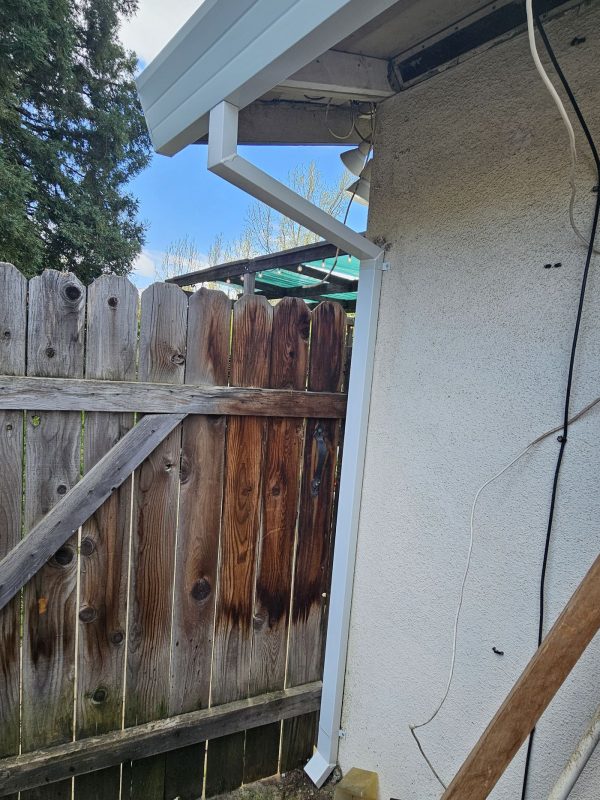 White downspout installed on the left side of a white garage door. The white downspout is attached to white gutters, which was also installed.