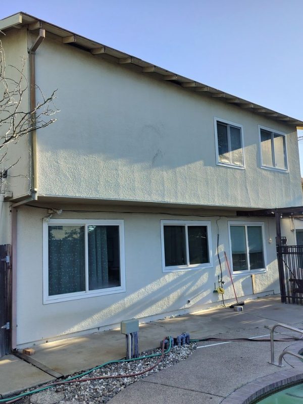Two-story home with a clean, stucco exterior without installed rain gutters and old downspouts positioned near a backyard pool