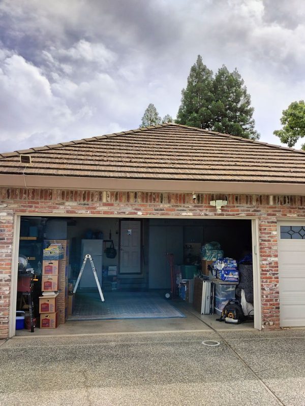 A brick house with an open garage. Brown gutters wrap around the perimeter of the home. A grey car is partially photographed