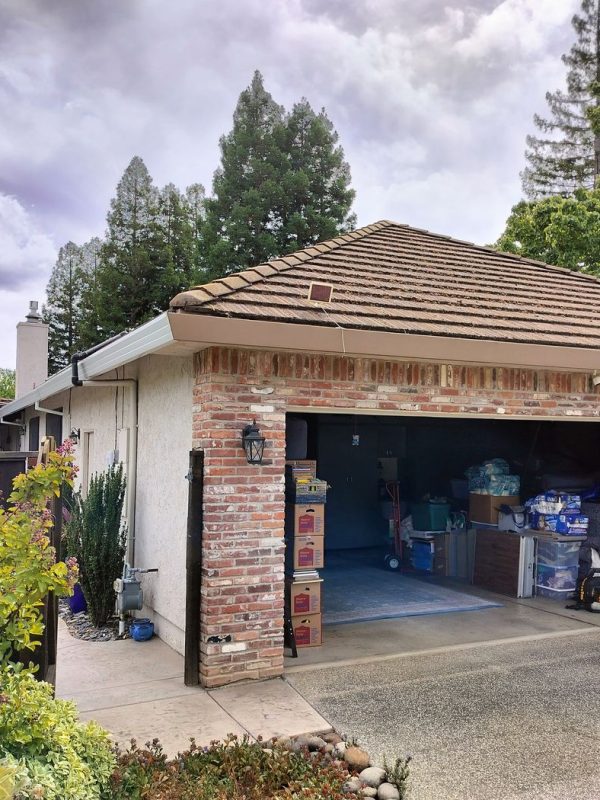 A brick house with an open garage. Brown and white gutters wrap around the perimeter of the home. A grey car is partially photographed