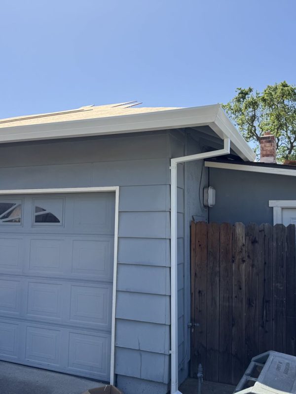 Grey home with white gutters and downspouts. The roof is under construction. There is a brown fence on the right side of the home.