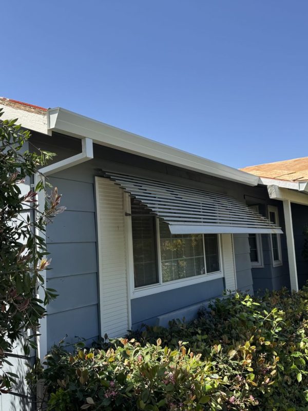 Front of the home, featuring a window with a stripped sun cover. There are newly installed gutters and downspouts.